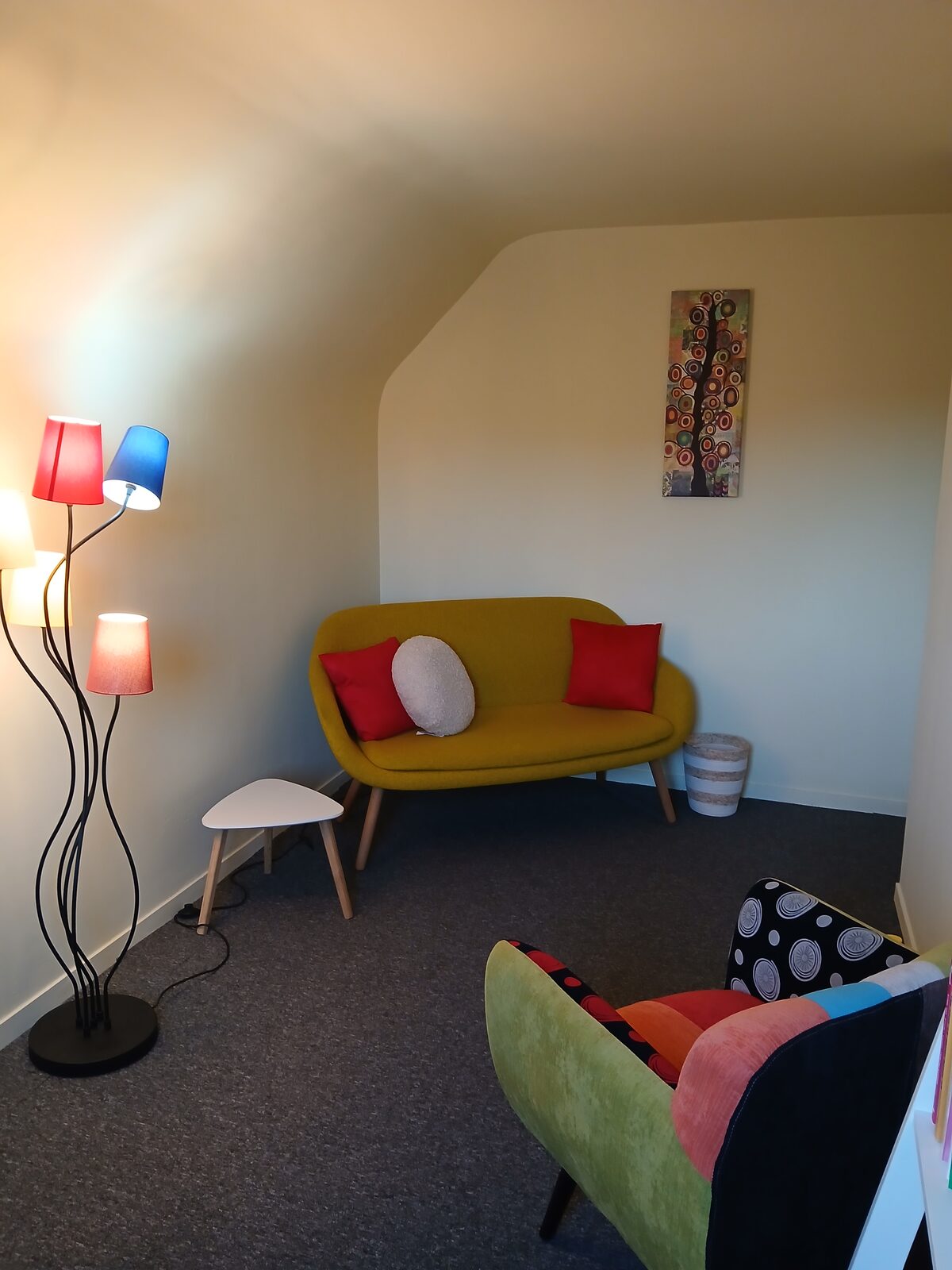 Le cabinet de consultation : un canapé moutarde, des lampes colorées et un espace lumineux et chaleureux.